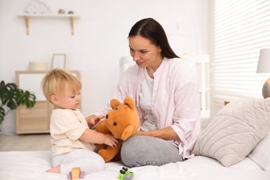 Photo of Mother with her cute little baby and toy on bed in room