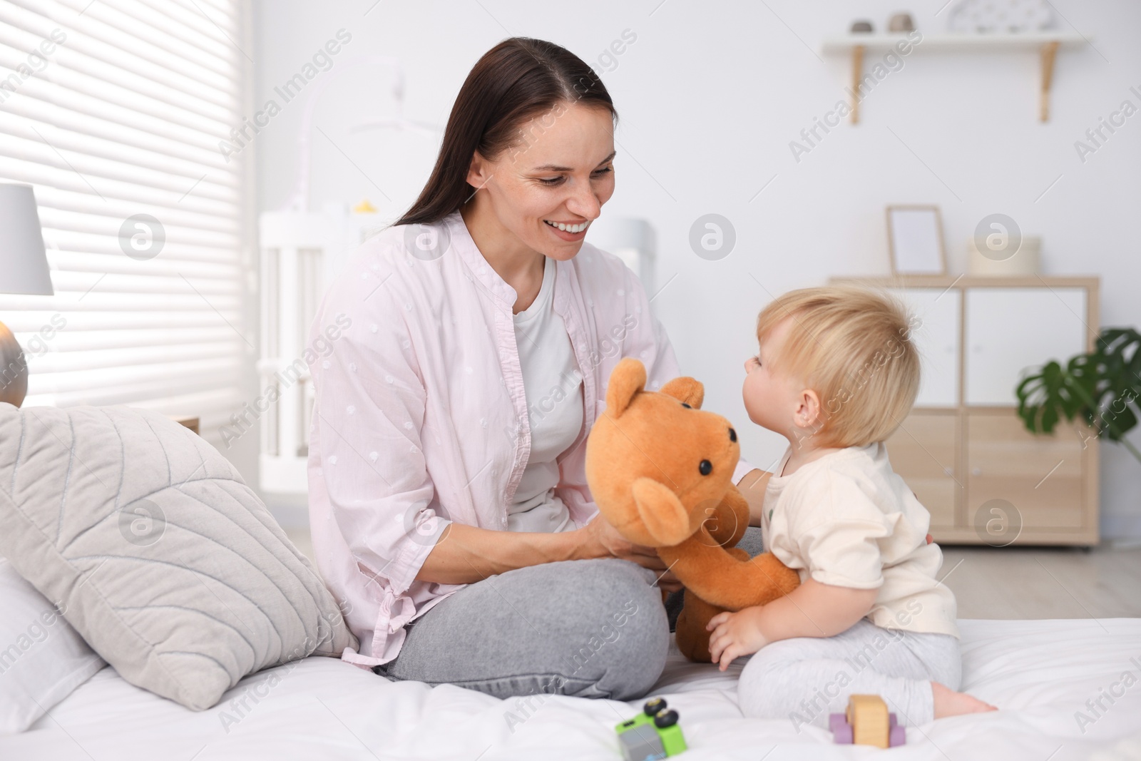 Mother with her cute little baby and toy on bed in room Photo of Mother with her cute little baby and toy on bed in room