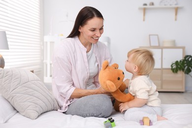 Photo of Mother with her cute little baby and toy on bed in room
