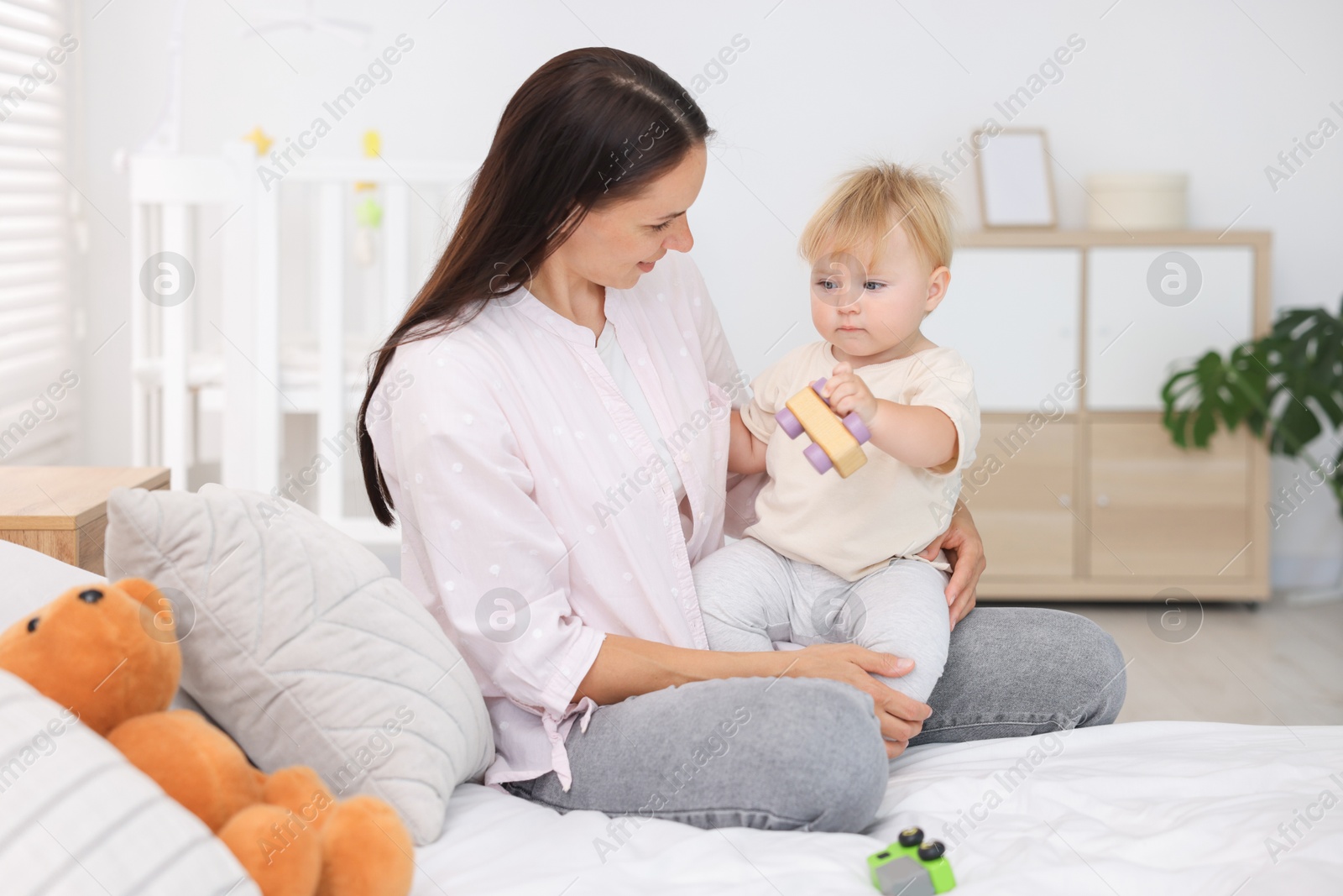 Mother and her cute little baby playing with toys on bed in room Photo of Mother and her cute little baby playing with toys on bed in room