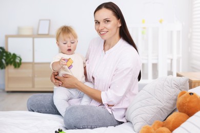 Photo of Mother and her cute little baby playing with toys on bed in room