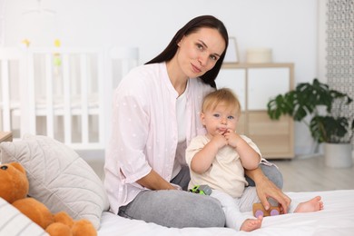 Photo of Mother and her cute little baby playing with toys on bed in room