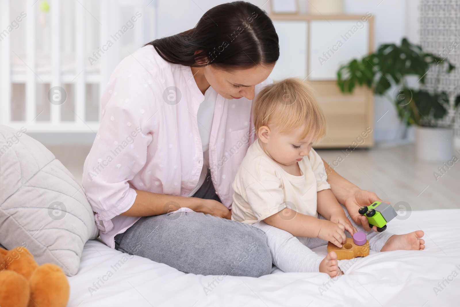 Mother and her cute little baby playing with toys on bed in room Photo of Mother and her cute little baby playing with toys on bed in room