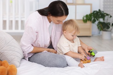 Photo of Mother and her cute little baby playing with toys on bed in room
