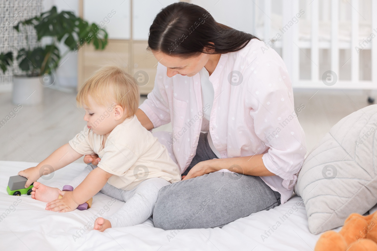 Mother and her cute little baby playing with toys on bed in room Photo of Mother and her cute little baby playing with toys on bed in room