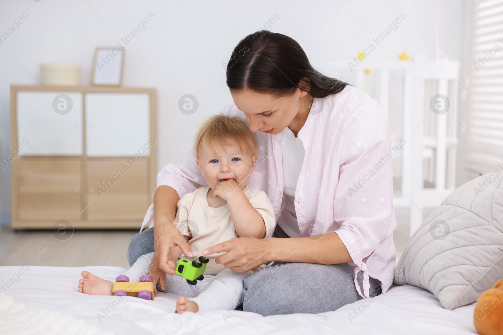 Mother and her cute little baby playing with toys on bed in room Photo of Mother and her cute little baby playing with toys on bed in room