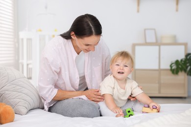 Photo of Mother and her cute little baby playing with toys on bed in room