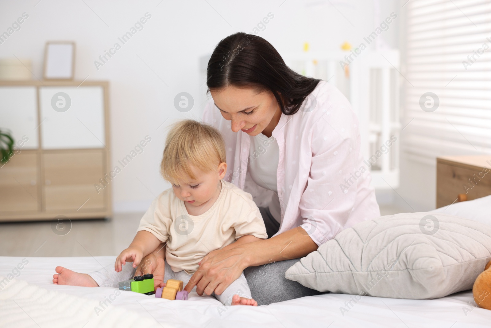 Mother and her cute little baby playing with toys on bed in room Photo of Mother and her cute little baby playing with toys on bed in room