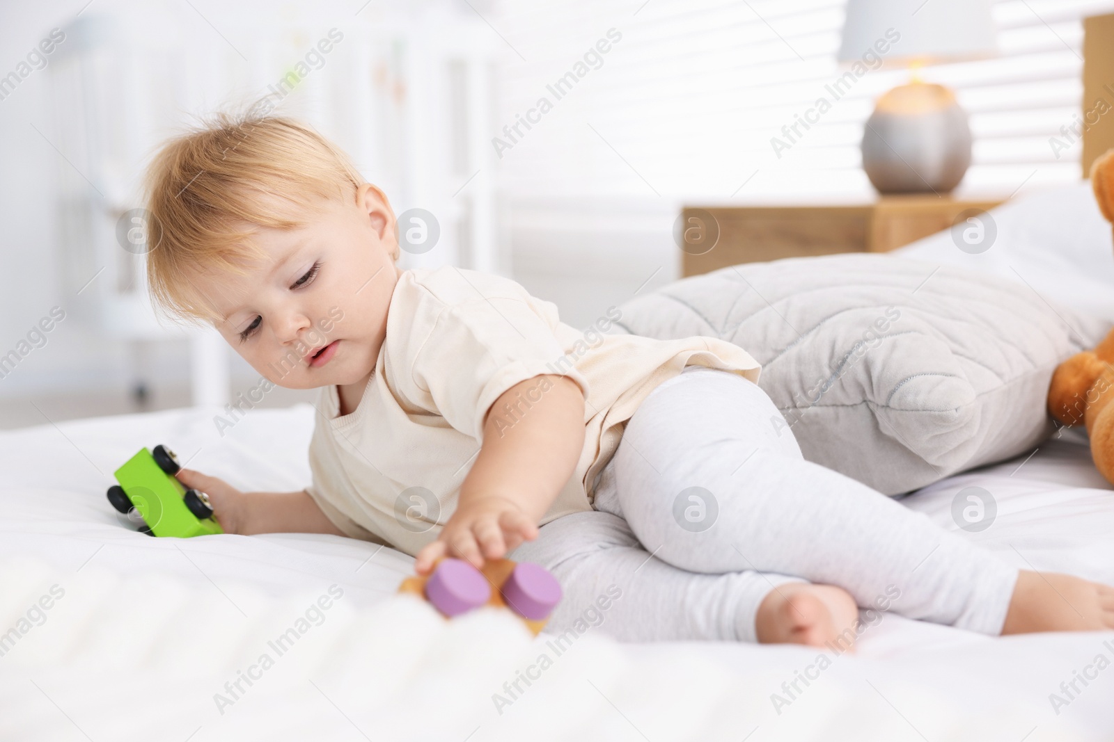 Cute little baby playing with toys on bed in room Photo of Cute little baby playing with toys on bed in room