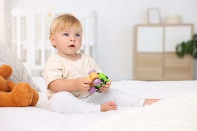 Photo of Cute little baby playing with toys on bed in room, space for text