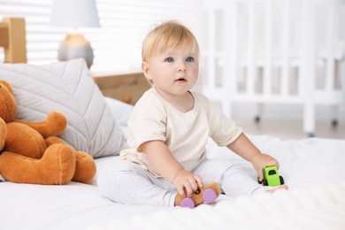 Photo of Cute little baby playing with toys on bed in room