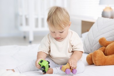 Photo of Cute little baby playing with toys on bed in room
