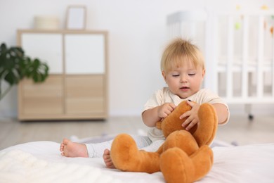 Photo of Cute little baby playing with toy on bed in room, space for text