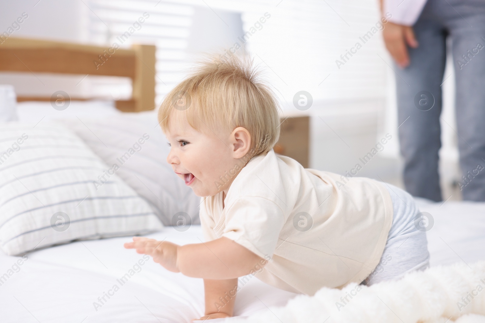 Cute little baby on bed and mother in room, selective focus Photo of Cute little baby on bed and mother in room, selective focus