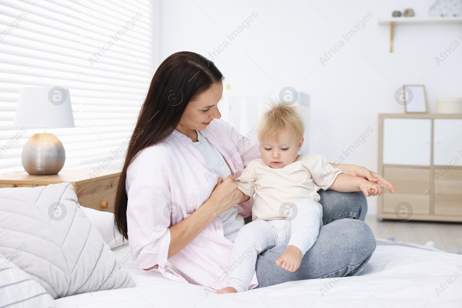 Mother and her cute little baby on bed in room Photo of Mother and her cute little baby on bed in room