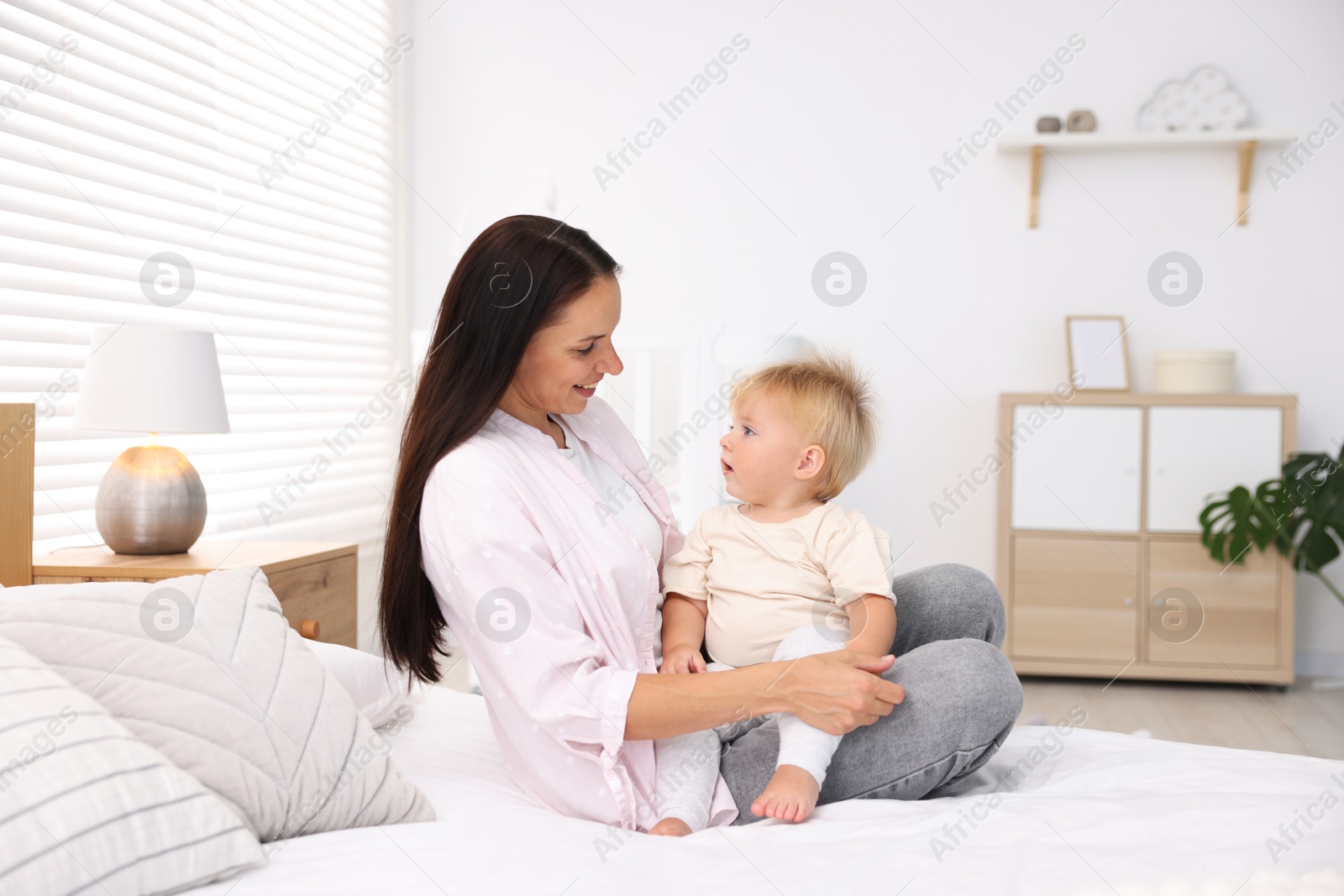 Mother and her cute little baby on bed in room Photo of Mother and her cute little baby on bed in room