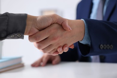 Photo of Business partners shaking hands at table indoors, closeup