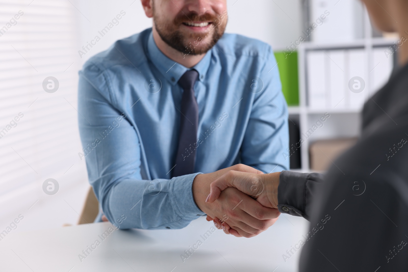 Photo of Business partners shaking hands at table indoors, closeup