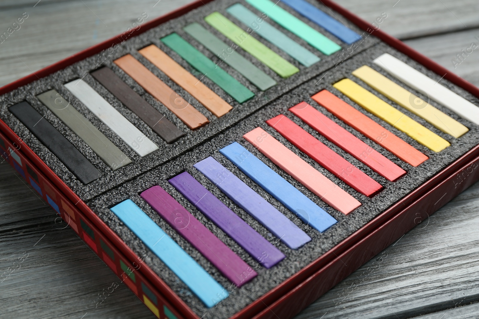 Photo of Colorful chalk pastels in box on wooden table, closeup