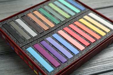 Photo of Colorful chalk pastels in box on wooden table, closeup
