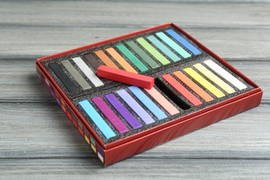 Photo of Colorful chalk pastels in box on wooden table, closeup