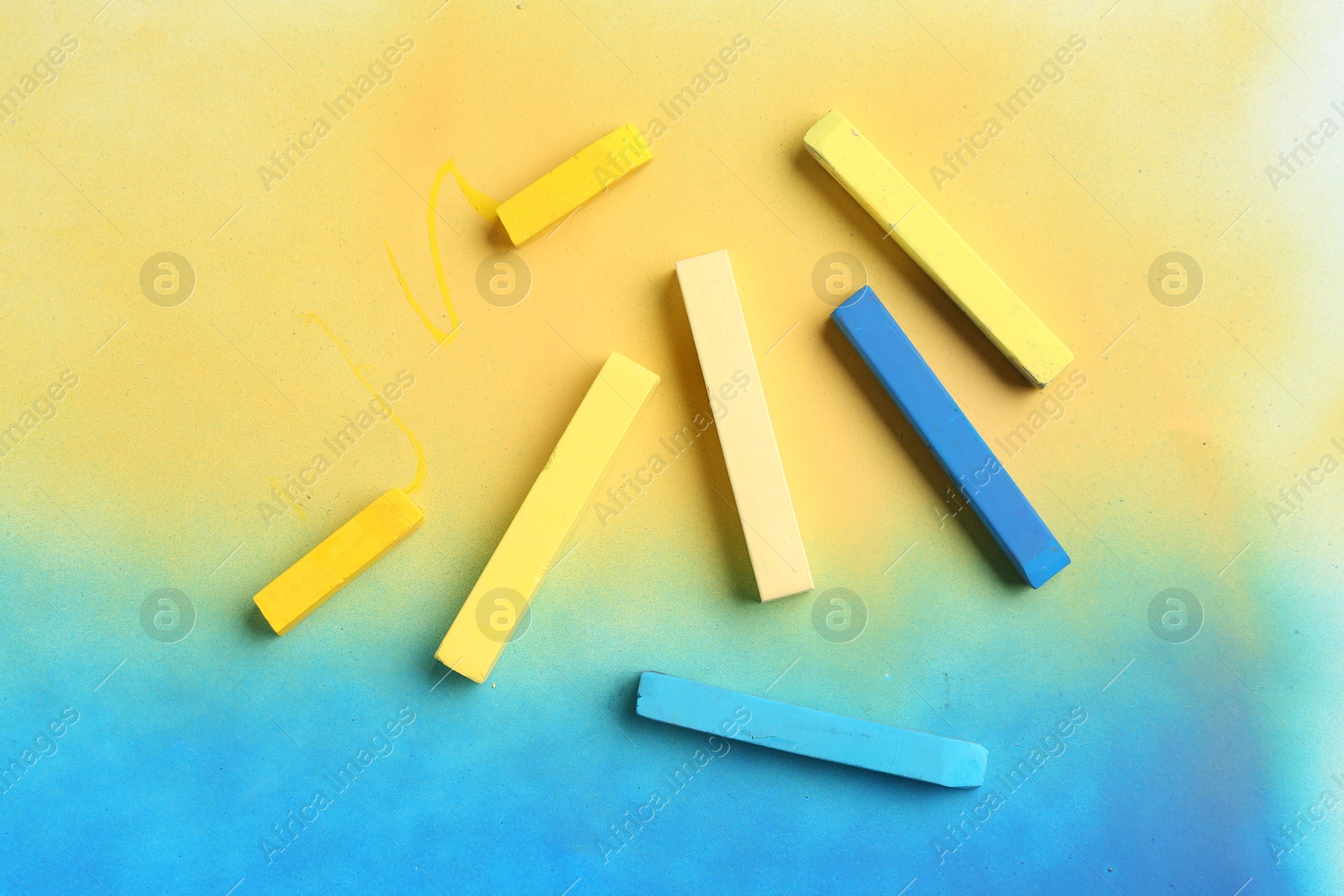 Photo of Yellow and light blue chalk pastels on color background, top view