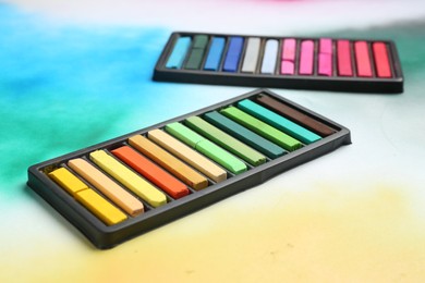 Photo of Colorful chalk pastels in trays on color background, closeup