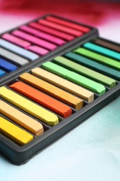 Photo of Colorful chalk pastels in trays on color background, closeup
