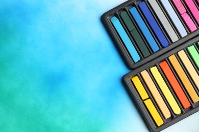 Photo of Colorful chalk pastels in trays on color background, flat lay. Space for text