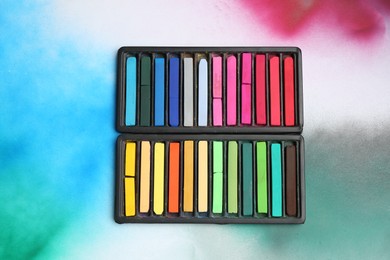 Photo of Colorful chalk pastels in trays on color background, top view