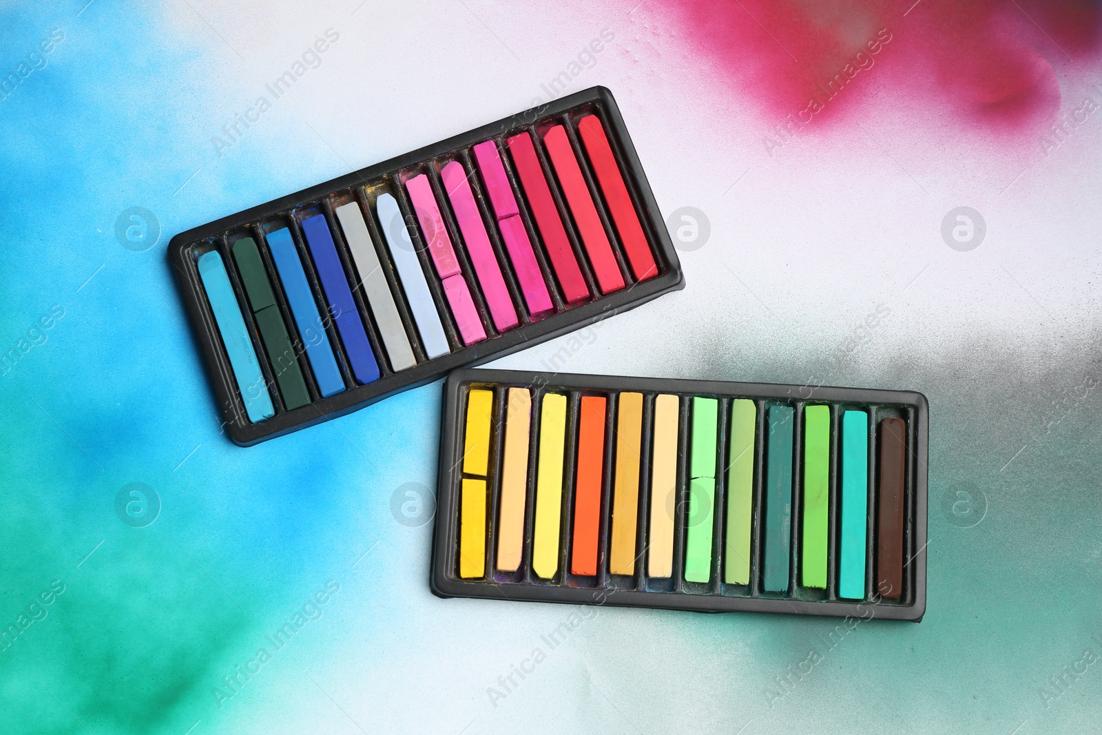 Photo of Colorful chalk pastels in trays on color background, flat lay