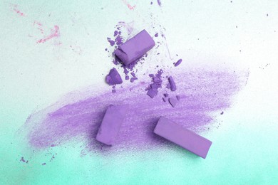 Photo of Violet chalk pastels and scribble on color background, flat lay