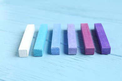Photo of Colorful chalk pastels on light wooden table, closeup