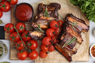 Photo of Roasted beef ribs with rosemary, tomatoes and other products on table, flat lay