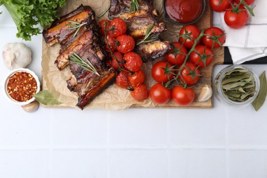 Photo of Roasted beef ribs with rosemary, tomatoes and other products on white tiled table, flat lay. Space for text