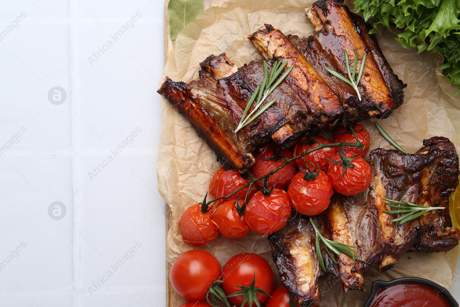 Roasted beef ribs with rosemary, tomatoes and other products on white tiled table, flat lay. Space for text Photo of Roasted beef ribs with rosemary, tomatoes and other products on white tiled table, flat lay. Space for text