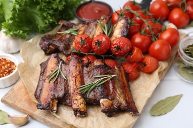 Photo of Roasted beef ribs with rosemary, tomatoes and other products on light table, closeup