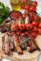 Photo of Roasted beef ribs with rosemary, tomatoes and other products on table, closeup