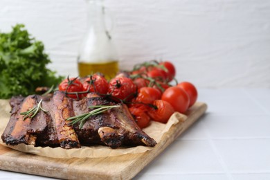 Photo of Roasted beef ribs with rosemary and tomatoes on white tiled table, closeup