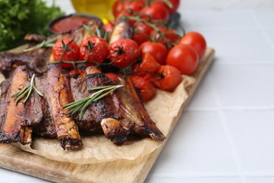 Photo of Roasted beef ribs with rosemary and tomatoes on white tiled table, closeup