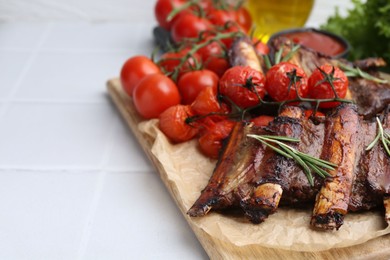 Photo of Roasted beef ribs with rosemary and tomatoes on white tiled table, closeup. Space for text