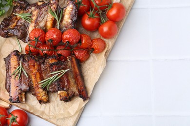 Photo of Roasted beef ribs with rosemary and tomatoes on white tiled table, flat lay. Space for text