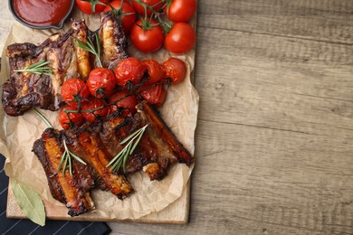 Photo of Roasted beef ribs with rosemary, tomatoes and sauce on wooden table, top view. Space for text