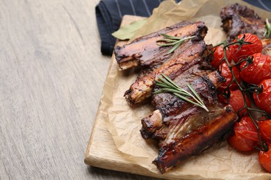 Photo of Roasted beef ribs with rosemary and tomatoes on wooden table, closeup. Space for text