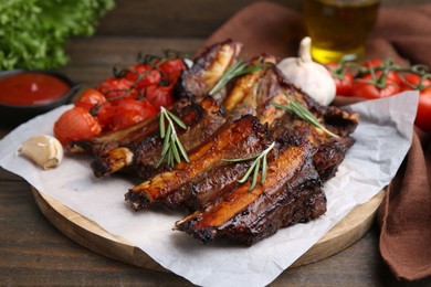Photo of Roasted beef ribs with spices and tomatoes on wooden table, closeup