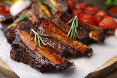 Photo of Roasted beef ribs with rosemary and tomatoes on table, closeup
