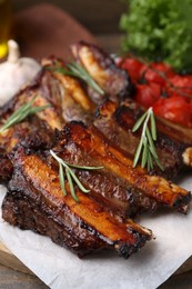 Photo of Roasted beef ribs with rosemary and tomatoes on table, closeup