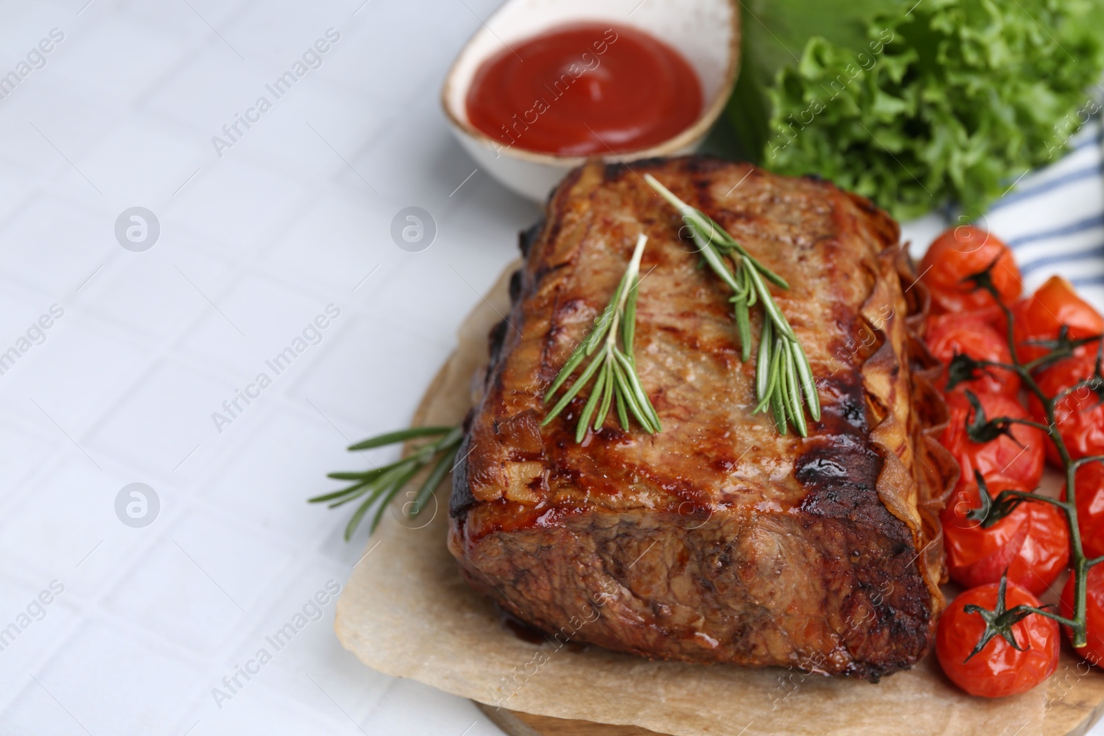 Delicious roast beef with rosemary, tomatoes, sauce and lettuce on white tiled table, closeup. Space for text Photo of Delicious roast beef with rosemary, tomatoes, sauce and lettuce on white tiled table, closeup. Space for text