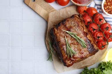 Photo of Delicious roast beef with rosemary, tomatoes and other products on white tiled table, flat lay. Space for text