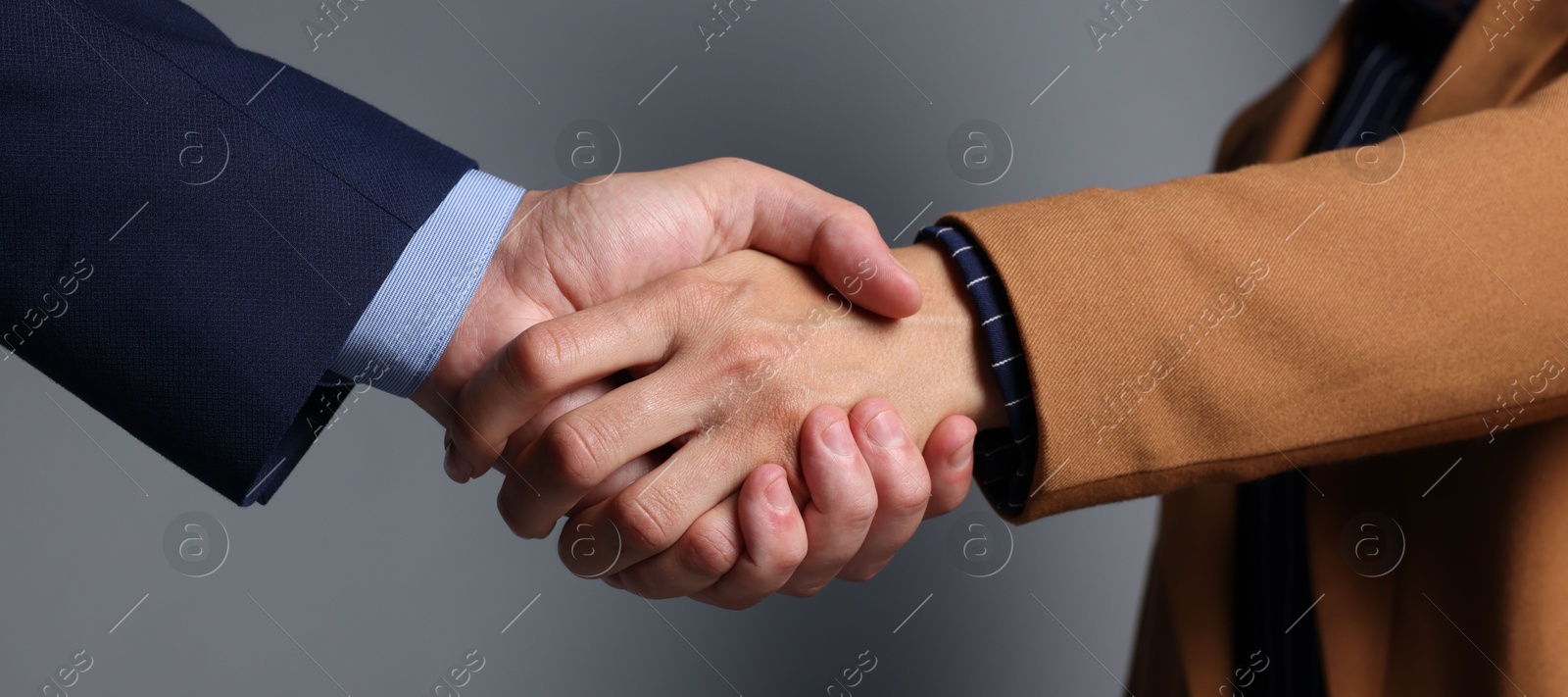 Photo of Business partners shaking hands on grey background, closeup